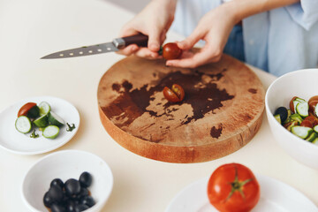 Woman preparing meal with fresh tomatoes and vegetables on wooden cutting board in domestic kitchen setting