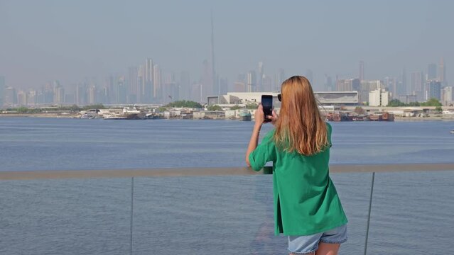 a young woman in a green T-shirt takes pictures of the Dubai cityscape on her phone
