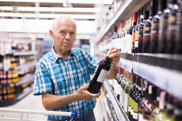 Mature senor choosing alcoholic drinks in supermarket