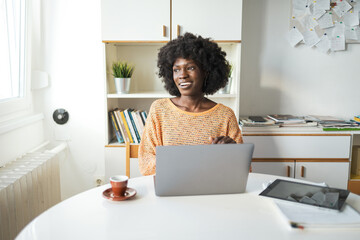 Thoughtful female freelancer sitting with laptop and digital tablet in home office