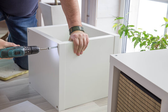 Man assembling purchased furniture in beautiful room with large window. Concept of DIY or furniture assembly services