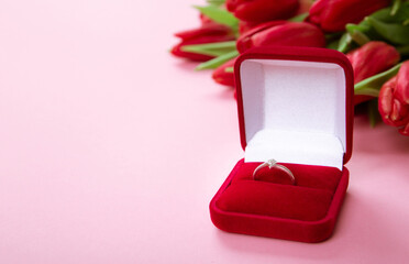 Big bouquet of red tulips with a diamond ring lais on the pink background. Symbol of love and the soul union. Jewelry gift or certificate to a jewelry shop. Holiday business card. Declaration of love