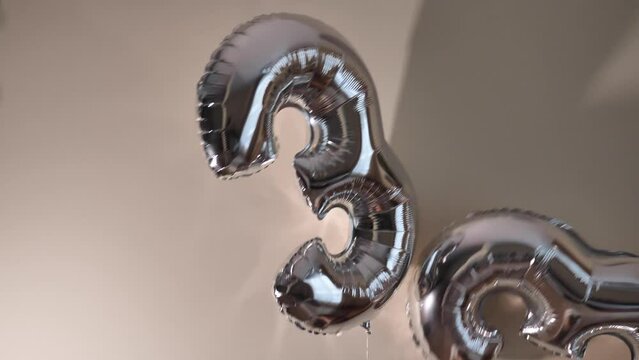 The silver balloons in the form of the number thirty-three against a beige wall.The two balloons are tied together at the bottom. Happy Birthday