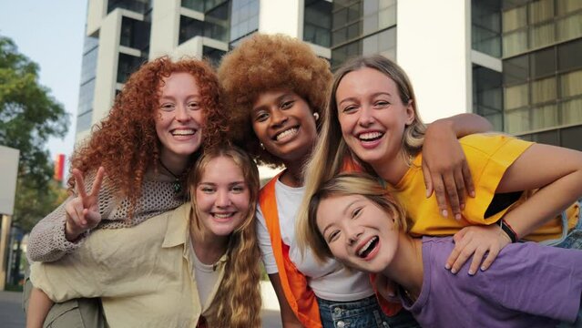 Social group of real young women are smiling and posing in front of a building, showing happy facial expressions. They are having fun while traveling as a community, enjoying leisure time together