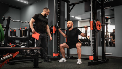 A large bearded man in the gym performs a squat exercise with a barbell. Preparation of a...