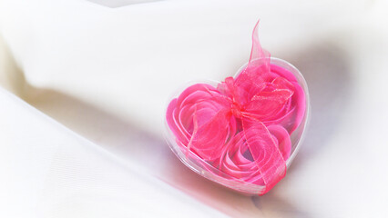 Valentine's Day concept. Pink roses in a heart-shaped box on satin beige fabric.