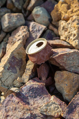 Rusty old tin can is located between the stones on the ground surface. Environmental protection theme. Vertical image.