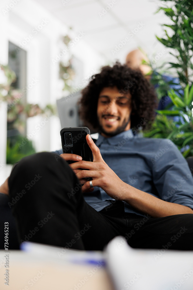 Poster smiling businessman relaxing in office, using smartphone to send message. young arab executive manag