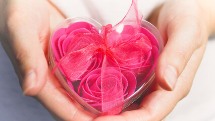 Valentine's Day concept. Pink roses in a heart-shaped box in female hands.