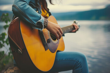 Woman playing acoustic guitar by lake, girl strumming guitar