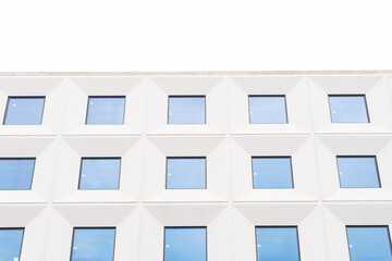 A minimalistic facade of a modern building with a geometric pattern of white structures and blue windows under a clear sky