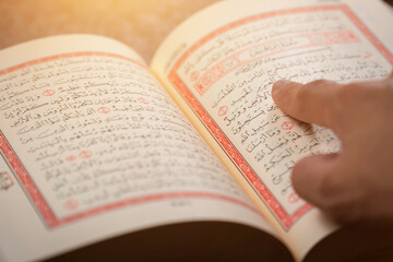 Quran (Koran) - close up of holy book of Muslims, with hand pointing ayat (Āyah), and shining light.