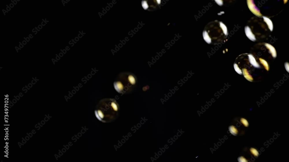 Poster colorful soap bubbles fly in empty space on isolated black background. golden lights. many rainbow t