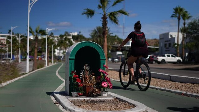 Catholic icon shrine blesses the cyclovia bike trail along the malecon in La Paz Mexico as two riders pass by.