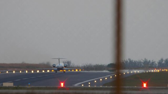 Private jet plane taking off, rear view through the fence. Runway lighting with landing lights