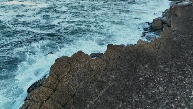 Aerial. White waves of the Atlantic Ocean crashing against a rocky shore