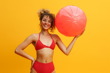 Funny young happy woman in red swimsuit having fun holding inflatable ball and going on summer...