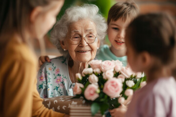 Happy senior woman receives presents from her grandchildren. Children make their grandmother a birthday surprise. Little kids give their grandma a gift card and a bouquet of flowers