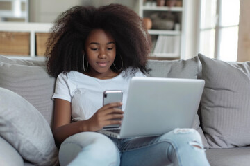 Young ethnic African American girl teenager uses laptop to chat with friends and use social networks on Internet sits on sofa with portable computer on lap. Digital addiction