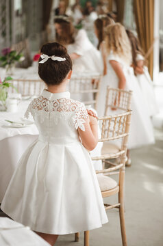 brunette girl with a high hairstyle and a bow stands with her back in a festive dress for a wedding, communion in a beautiful restaurant, against the background of other girls in formal dresses