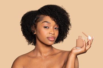 Serene young black woman presenting liquid foundation bottle