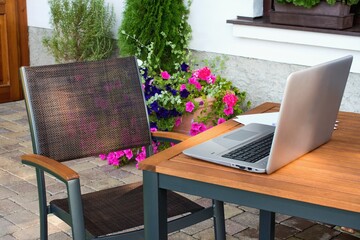 Home working place with laptop in the beautiful summer terrace and blooming garden