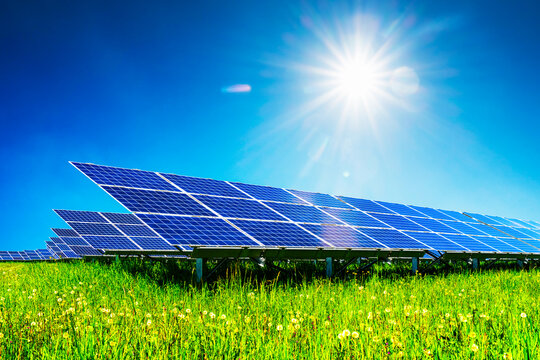 Blue solar panels under deep blue sky with bright sun with sunbeams. Alternative energy concept