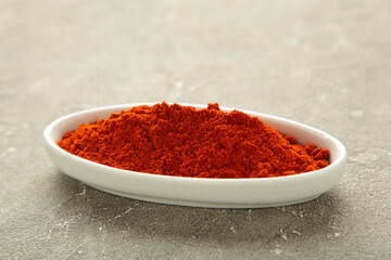 Red sweet paprika powder on plate on grey background