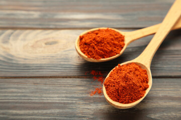 Powder paprika with wooden spoon on brown wooden background