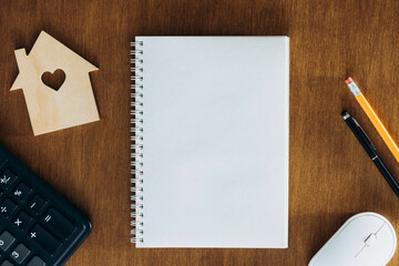 Blank notebook, calculator and model of a house on a wooden table. Planning to buy a home,...