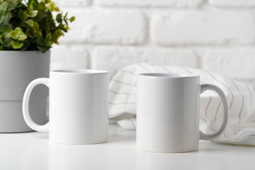 Two mugs on white table against brick wall background