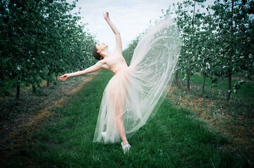 A beautiful girl in an airy long dress dances among a blooming apple orchard. Spring