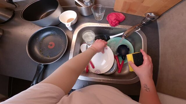 Washing dishes top view. Hands female first person view washing lot of dishes at home in kitchen sink. Housework and housekeeping. Household hassle and domestic clean up. POV wash housewares. 