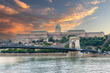 Photo sur Plexiglas Széchenyi lánchíd Szechenyi Chain bridge over the Danube River in the city of Budapest. Urban landscape with old buildings, St. Stephens Basilica and opera domes. Reddish sky and flying birds in the background. Hungary