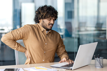 Obraz premium Indian businessman in casual wear focused on work with a laptop in a contemporary office setting, embodying professionalism.