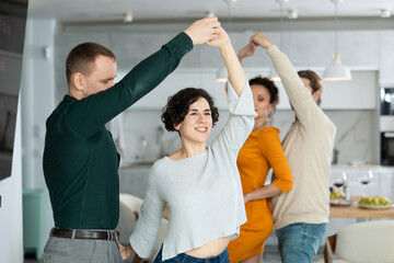Two married couples dance during holiday, have fun, move and jump in dining room. Family event is...