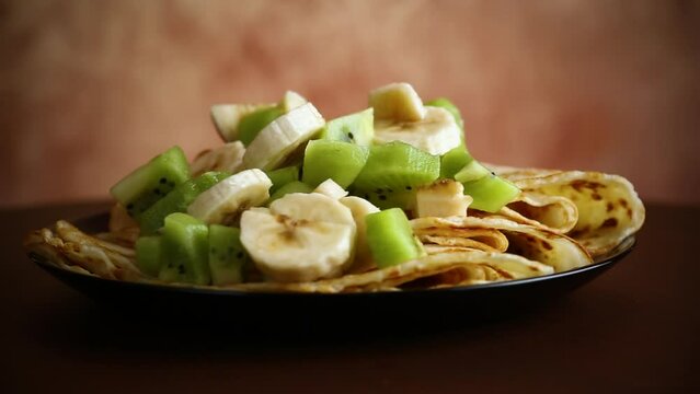 cooked thin pancakes with bananas and kiwi on a light wooden table
