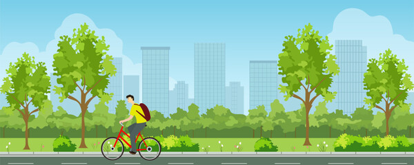 Cyclist rides a bicycle along the path of a city park against the backdrop of the city landscape. Landscape of a city park with green trees and tall buildings in the background. © LoveSan