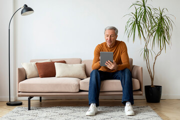 Relaxed mature man chilling at home, using tablet - obrazy, fototapety, plakaty