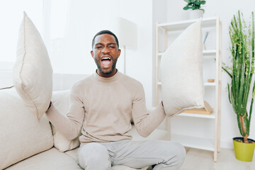 Relaxed African American man sitting on a comfortable sofa in his modern apartment, enjoying a...
