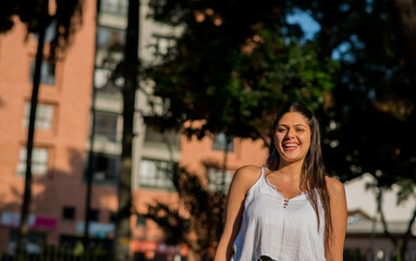 mujer joven sonriendo mientras mira a la camara y esta en un parque de la ciudad 