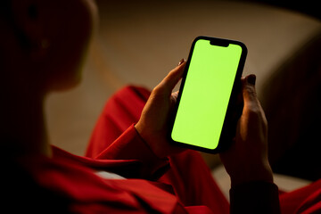 An over-the-shoulder view captures a woman using a smartphone with a green screen, potentially...