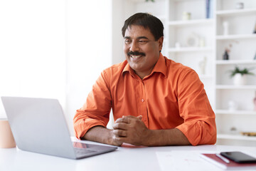 Smiling eastern middle aged businessman working on laptop