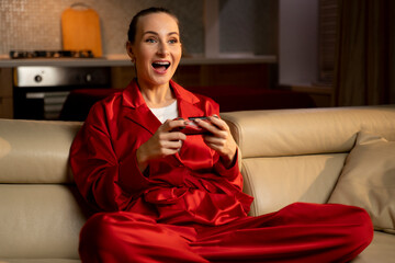 A woman appears ecstatic and surprised while actively playing video games, seated on a beige couch...