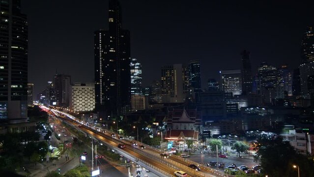 dynamic energy of a busy city at night, highlighting the steady flow of traffic alongside the glowing lights of towering skyscrapers. bangkok thailand