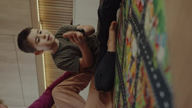 Little boy with his grandmother playing toy cars on play mat sitting on the floor. City street map rug. Kids at home or daycare.Little boy with his grandmother