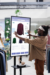 Online store buyer looks for clothes on touch screen board in clothing store, shopping for fashion...