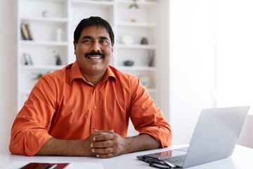 Portrait mature indian man posing at workplace at home office