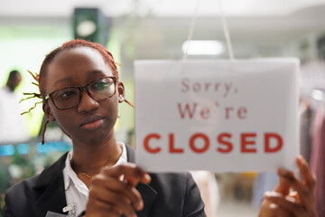 Clothing shop african american woman manager hanging sorry we are closed sign on window. Apparel...