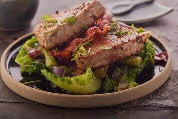 Seared tuna steaks with crispy bacon on a bed of vegetables and garnished with herbs. - obrazy, fototapety, plakaty